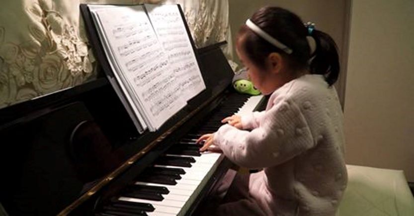 Маленькая девочка как взрослая играет на пианино и читает с нотного листа